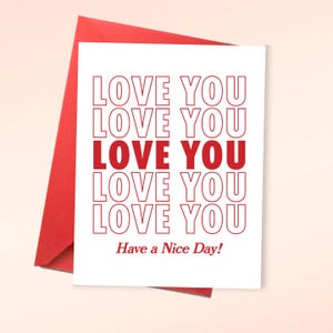 May include: A white greeting card with the words "LOVE YOU" repeated in red, with one instance in a solid red font. The phrase "Have a Nice Day!" is printed at the bottom in red. The card is inside a red envelope.