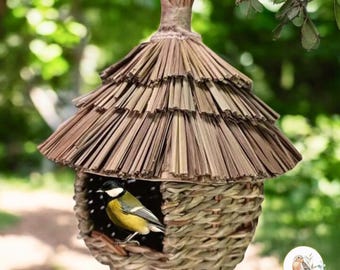 May include: A woven bird feeder with a thatched roof, hanging from a tree branch. A small yellow and black bird is perched inside the feeder.