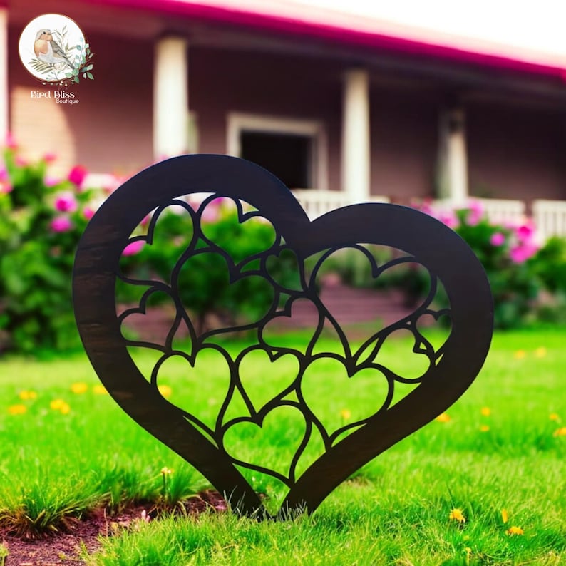 May include: A black metal heart-shaped garden stake with a cut-out design of multiple hearts. The stake is placed in a green grassy lawn with a blurred background of a house and flowers. The stake is from Bird Bliss Boutique.