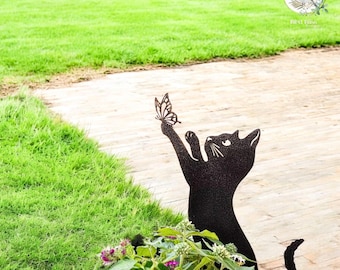 May include: A black metal cat garden stake with a butterfly on its paw. The cat is reaching up towards the butterfly. The garden stake is placed in front of a green lawn and a stone pathway.