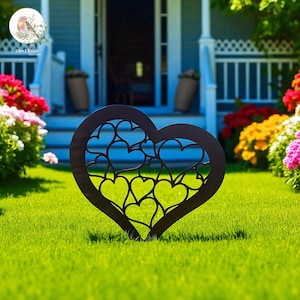 May include: A dark brown metal heart-shaped garden stake with a cut-out heart design. The stake is placed in a green lawn with a house and flowers in the background. The garden decor is a charming addition to any outdoor space.