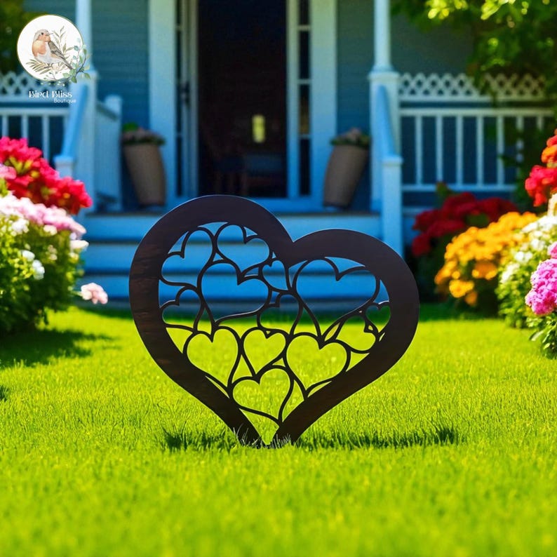 May include: A dark brown metal heart-shaped garden stake with a cut-out heart design. The stake is placed in a green lawn with a house and flowers in the background. The garden decor is a charming addition to any outdoor space.