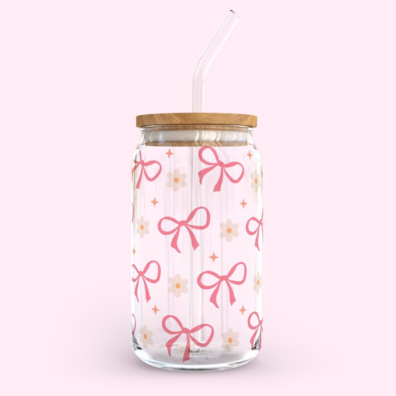May include: A clear glass jar with a wooden lid and a pink and white bow pattern. The jar has a clear glass straw.
