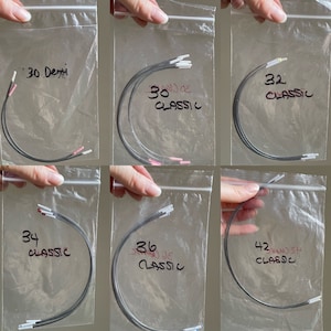 Pode incluir: Seis sacos de plástico transparentes, cada um contendo um conjunto de cordas de guitarra pretas com pontas de cores diferentes. Os sacos são etiquetados com a calibre das cordas: 30 Demi, 30 Classic, 32 Classic, 34 Classic, 36 Classic e 42 Classic.