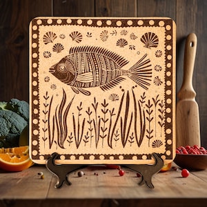 May include: A brown cork trivet with a decorative design of a fish swimming in a bed of seaweed. The trivet has a brown border with white polka dots and is on a wooden stand.