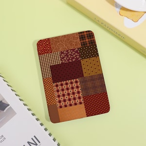 May include: A rectangular e-reader cover featuring a patchwork design of various brown, tan, and deep red fabric patterns. The surface displays a mix of small stars, plaid, polka dots, and swirling line motifs arranged in a grid-like composition.