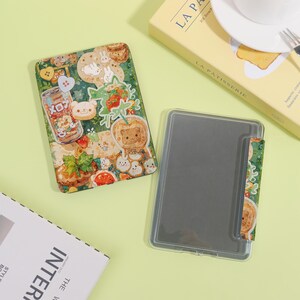 May include: A green and clear tablet case with a colorful, cartoon-style design featuring bears, strawberries, and other food-themed illustrations. The case is open, revealing the tablet screen. The design includes the word "メロン" on a can.