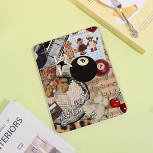 May include: A decorative tablet case featuring a collage of teddy bears, a disco ball, a star, a pool ball, and the word "LUCKY". The case has a mix of textures and colors, including a leopard print.