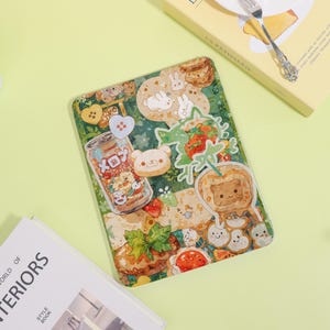 May include: A rectangular, clear case with a whimsical design featuring cartoon bears, bunnies, strawberries, and a soda can with the text "xox". The case has a green and beige background with a variety of cute illustrations.