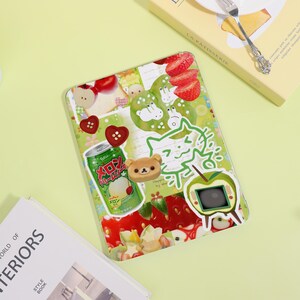 Könnte beinhalten: Eine Tablet-Hülle mit einer Collage aus bunten Aufklebern. Das Design umfasst Erdbeeren, grüne Äpfel, einen Bären und eine japanische Limonadendose. Die Hülle hat ein klares, glänzendes Finish und einen hellgrünen Hintergrund.