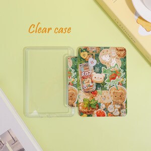 May include: A clear phone case with a colorful design featuring cartoon characters, strawberries, and a soda can. The text "Clear case" is printed in orange. The case is rectangular and has a transparent frame.