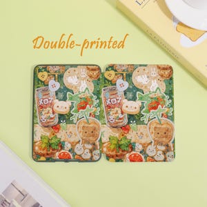 May include: Two decorative phone cases with a whimsical design. Each case features a repeating pattern of cartoon bears, bunnies, strawberries, and soda cans. The text "Double-printed" is in orange script above the cases.