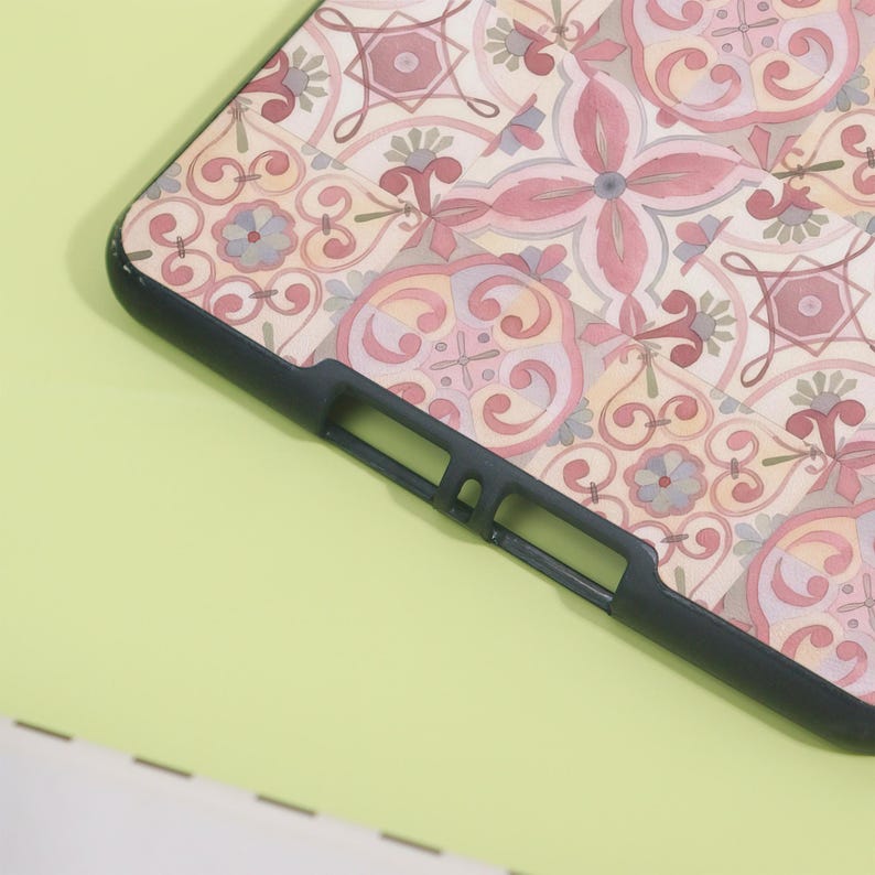 K&ouml;nnte beinhalten: Eine schwarze Handyh&uuml;lle mit einem farbenfrohen, verzierten Muster in Rosa-, Beige- und Graut&ouml;nen. Das Design weist florale und geometrische Elemente auf. Die H&uuml;lle wird auf einer hellgr&uuml;nen Oberfl&auml;che gezeigt.