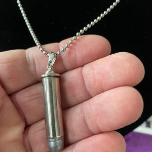 May include: A silver bullet pendant necklace with a silver chain. The bullet is approximately 5 cm long and has a rounded tip.