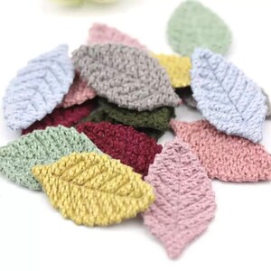 May include: A selection of fabric leaf appliques in a variety of colours. The leaves are in shades of yellow, pink, blue, green, and burgundy. The leaves have a detailed, stitched texture, and are likely for crafting or embellishment.