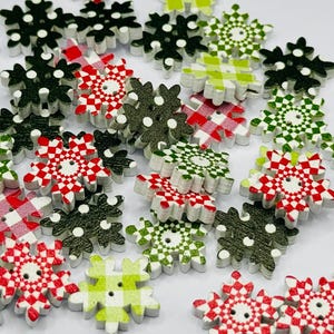 May include: A selection of wooden snowflake buttons in various colours and patterns. The buttons feature red and white checked, green and white checked, and solid black designs. Each button has a small hole in the centre for sewing.