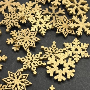 Pode incluir: Uma coleção de pequenos recortes de flocos de neve de madeira dourada. Os flocos de neve apresentam vários designs com detalhes intrincados e uma textura natural de grão de madeira. Ideal para artesanato e decorações de férias.