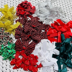 May include: A collection of small decorative bows in various colours and patterns, including red, green, gold, silver, white, and black and red buffalo plaid. These bows are made from satin, metallic, and textured ribbons for craft projects.