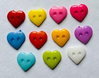 May include: A selection of heart-shaped buttons in a range of colours: red, yellow, pink, blue, orange, purple, green, and white. Each button has two holes for sewing and a glossy finish, ideal for craft projects.