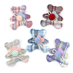 May include: Five plaid teddy bear embellishments in blue, pink, and purple hues. Each bear features a small pom-pom and heart-shaped accents. The bears are arranged on a white background, ideal for craft projects.