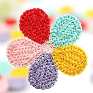 May include: A close-up of a crocheted flower with five petals in vibrant colours: red, turquoise, yellow, pink, and purple. The centre is a cluster of white threads. The flower is set against a soft, blurred background, suggesting a craft item.
