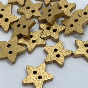 Può includere: Una collezione di bottoni a forma di stella color oro. Ogni bottone ha due fori per cucire. I bottoni hanno una superficie strutturata e sono sparsi su uno sfondo bianco. Questi bottoni decorativi sono ideali per progetti di artigianato.