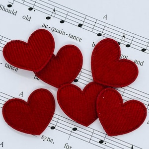 Könnte beinhalten: Sechs rote herzförmige Stoffflicken auf einem Notenblatt. Die Herzen haben eine strukturierte Oberfläche und sind leicht überlappend angeordnet. Die Noten sind schwarz auf weißem Hintergrund.