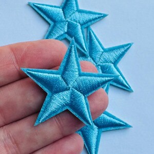 May include: Four turquoise star-shaped embroidered patches. The patches are a vibrant shade of blue and have a textured, stitched appearance. These patches are ideal for adding a decorative touch to clothing, bags, or other fabric items.