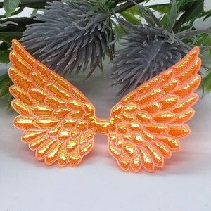 May include: A pair of bright orange, iridescent angel wings with a textured, scale-like feather pattern. The wings are symmetrical, featuring a scalloped edge and a vibrant, reflective finish that catches the light, creating a shimmering effect.