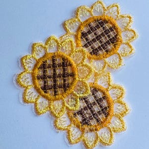 Peut inclure: Trois appliqués brodés en forme de tournesol. Chaque appliqué présente un motif de pétales jaunes et blancs entourant un centre brun quadrillé. Les appliqués sont probablement destinés à l'artisanat ou à l'embellissement.