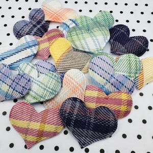May include: A collection of heart-shaped fabric patches in various plaid patterns. The patches feature a range of colors, including blue, green, yellow, and pink. The hearts are arranged on a white surface with black polka dots.