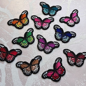 May include: A selection of embroidered butterfly patches in a range of colours, such as orange, green, pink, and blue. Each patch has detailed wing patterns, a black border, and white accents.