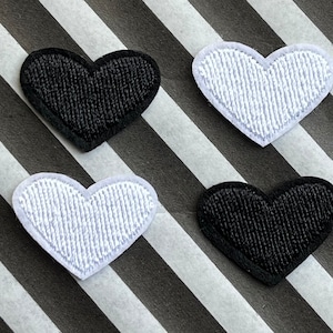 May include: Four heart-shaped patches, two black and two white, arranged on a black and white striped background. The hearts have a textured, stitched appearance. These patches could be used for clothing or craft projects.
