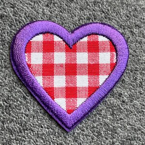 Pode incluir: Patch bordado em forma de coração com borda roxa. O centro apresenta um padrão xadrez vermelho e branco, que lembra uma toalha de piquenique. Adequado para roupas, bolsas ou outros artigos de tecido.