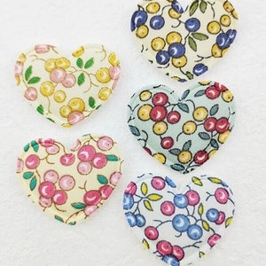 May include: Five heart-shaped fabric patches with floral patterns. The patches feature various color schemes, including pink, yellow, and blue berries with green leaves on a light background. These patches are suitable for crafts.
