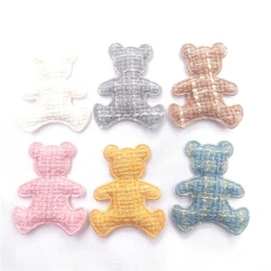 May include: Six fabric teddy bear embellishments in cream, grey, brown, pink, yellow, and blue. Each bear has a woven texture and is designed with arms and legs outstretched.
