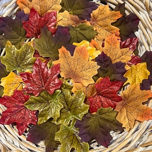 Peut inclure: Un assortiment de feuilles d'érable artificielles aux couleurs automnales, rouge, orange, jaune et vert, disposées dans un panier en osier. Les feuilles présentent des nervures détaillées, idéales pour la décoration.