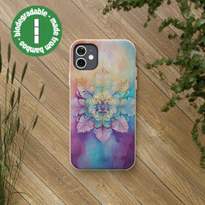 Può includere: Una custodia per telefono con un design a mandala colorato. La custodia è realizzata in bambù ed è biodegradabile. Il mandala è un design circolare con dettagli intricati e una varietà di colori, tra cui rosa, blu e viola.