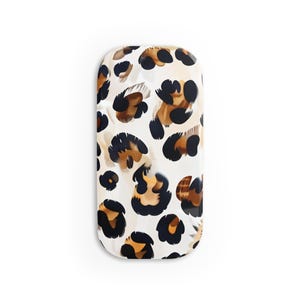 May include: A white oval-shaped phone case with a leopard print pattern in shades of brown, black, and white.