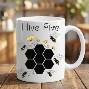Puede incluir: Taza de cerámica blanca con el texto "Hive Five". La taza presenta un diseño de panal con flores amarillas y abejas de dibujos animados. La taza tiene un asa blanca.