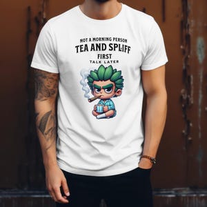 Puede incluir: Camiseta blanca con una ilustración de dibujos animados de una persona sosteniendo una taza y fumando un cigarrillo. El texto en la camiseta dice "Not a morning person Tea and Spliff First Talk Later".