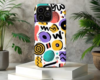 以下が含まれることがあります： 白のiPhoneケース。カラフルな抽象的なデザインで、紫、黄色、ターコイズ、赤、黒の色合いで、円やジグザグなど様々な形が描かれています。白いプラットフォームの上に置かれ、背景には緑の植物があります。