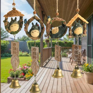 Puede incluir: Cuatro campanillas de viento colgantes con un personaje de dibujos animados. Cada campanilla tiene una campana, una hoja de madera o una placa con texto japonés y una figura en un nido o casa. Las figuras son grises, crema y marrones.