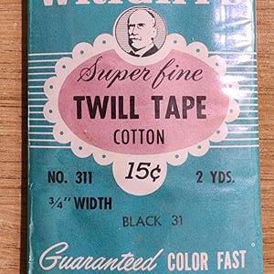Könnte beinhalten: Vintage-Packung mit Wright's Superfine Twill Tape in Schwarz. Die Verpackung hat ein türkis-rosa Etikett mit dem Text "TWILL TAPE COTTON" und "Guaranteed COLOR FAST". Das Band ist 1,9 cm breit.