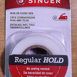 May include: A package of Singer iron-on fusing web. The red and white packaging features the Singer logo and product details. The product is a roll of white fusible tape, measuring 15 yards by 3/4 inches.