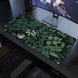 May include: A rectangular desk mat featuring a dark green background with a repeating pattern of green leaves and white flowers. The mat is designed to protect the desk surface and provide a smooth surface for a mouse and keyboard.