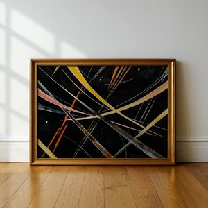 May include: Abstract art print in a gold frame. The artwork features a black background with intersecting lines in shades of yellow, orange, and pink. The lines create a dynamic, energetic composition. The framed art is displayed against a white wall and wooden floor.