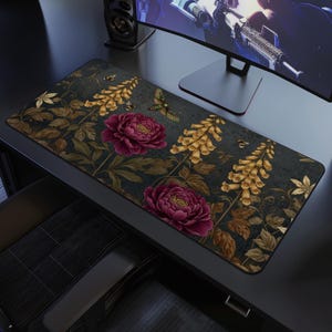 May include: A rectangular desk mat featuring a dark background with a floral design. The design includes burgundy peonies, yellow flowers, and green and brown leaves. The mat is placed on a black desk, with a computer monitor and speaker in the background.