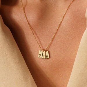 May include: A gold chain necklace with three small rectangular pendants, each with a letter engraved on it. The letters are "R", "T", and "M".
