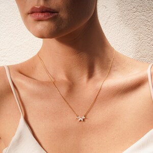 May include: A gold chain necklace with a delicate pendant featuring a cluster of small, clear marquise-shaped stones.